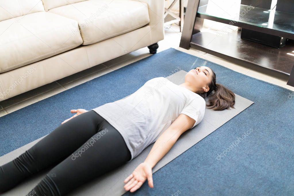 hispanic woman practicing yoga dead body pose on yoga mat at home