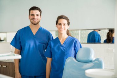 Portrait of smiling male and female dentists in scrubs standing at dental clinic
