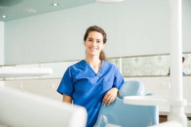 Gülümseyen genç kadın dişçi koltuğu diş kliniği tarafından ayakta portresi