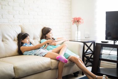 Küçük kız evde kanepede otururken uzaktan kumandalı TV Kanal seçme