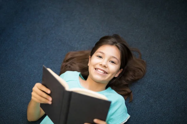 Menina Feliz Segurando Livro Aberto Enquanto Deitado Tapete Casa — Fotografia de Stock