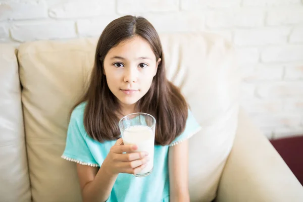 在家里坐在沙发上的快乐的孩子女孩拿着玻璃杯牛奶 — 图库照片