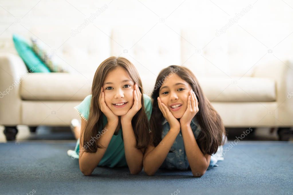 Young sisters lying on floor mat and having fun while spending time together at home