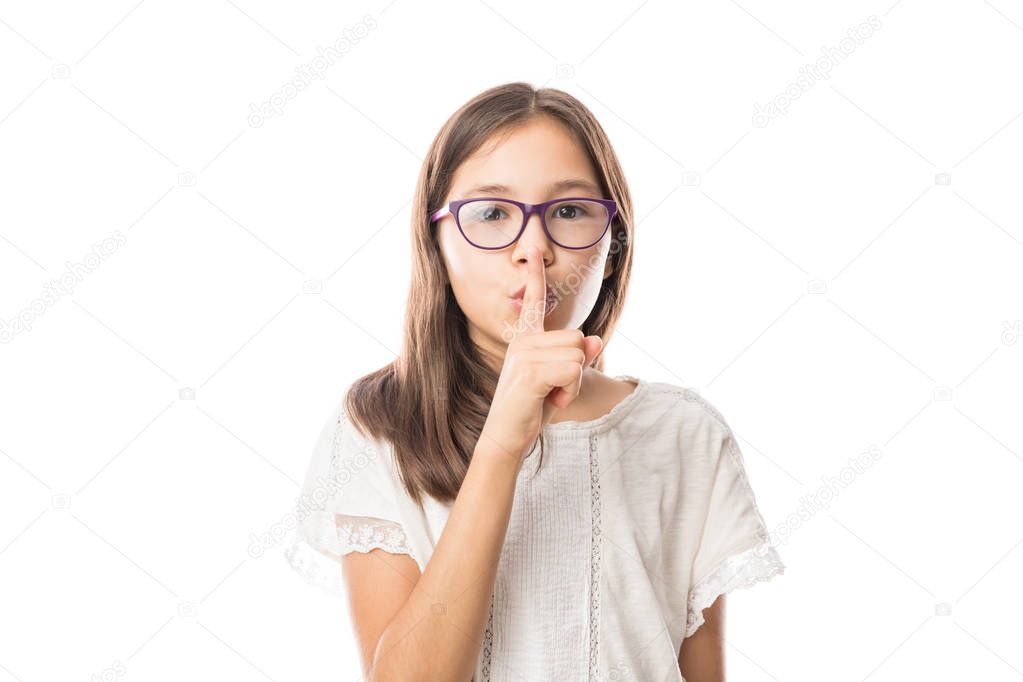portrait of adorable girl in spectacles putting finger up to lips and showing shh sign isolated on white background
