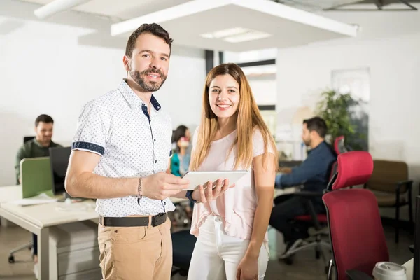 Portrait of business man and woman looking at camera while standing with digital tablet in office