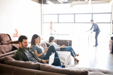 Grup kanepede oturan ve lounge Oda arkada tablet tenis oynayan meslektaşları ile dizüstü bilgisayarlar ve dijital tablet kullanarak iş adamları 