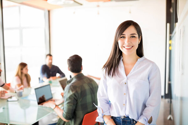 Young businesswoman in casual clothes at modern startup meeting room with colleagues working on background