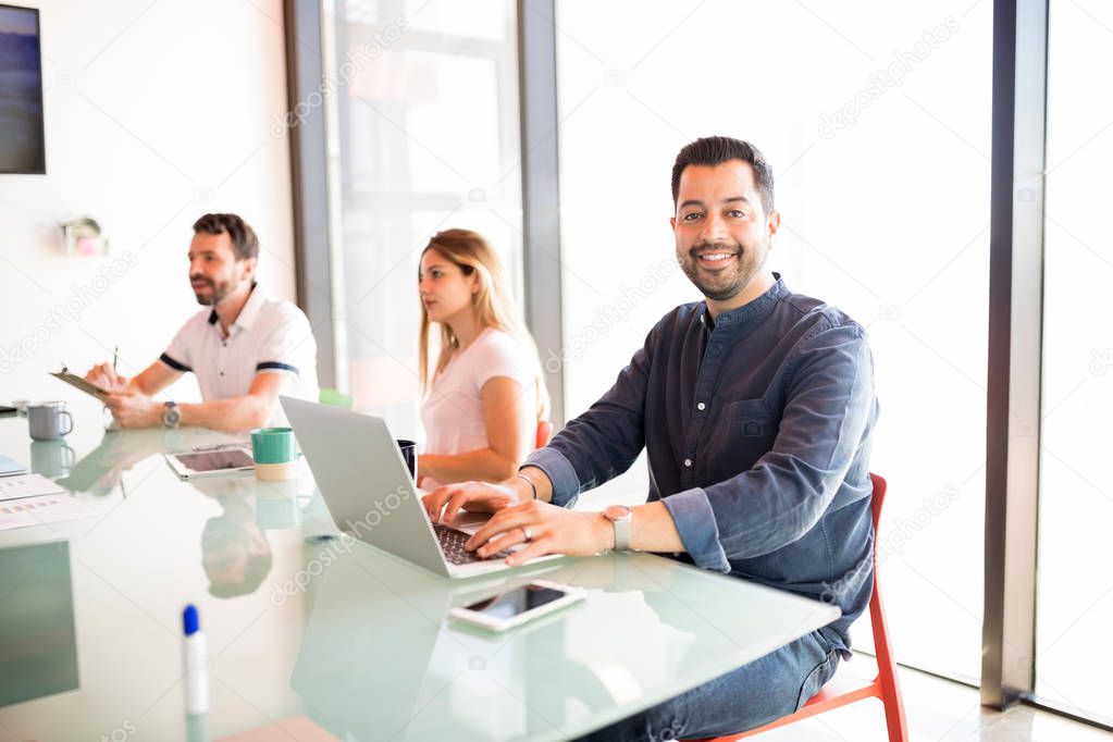 Portrait of good looking hispanic business man sitting with coworkers in meeting room