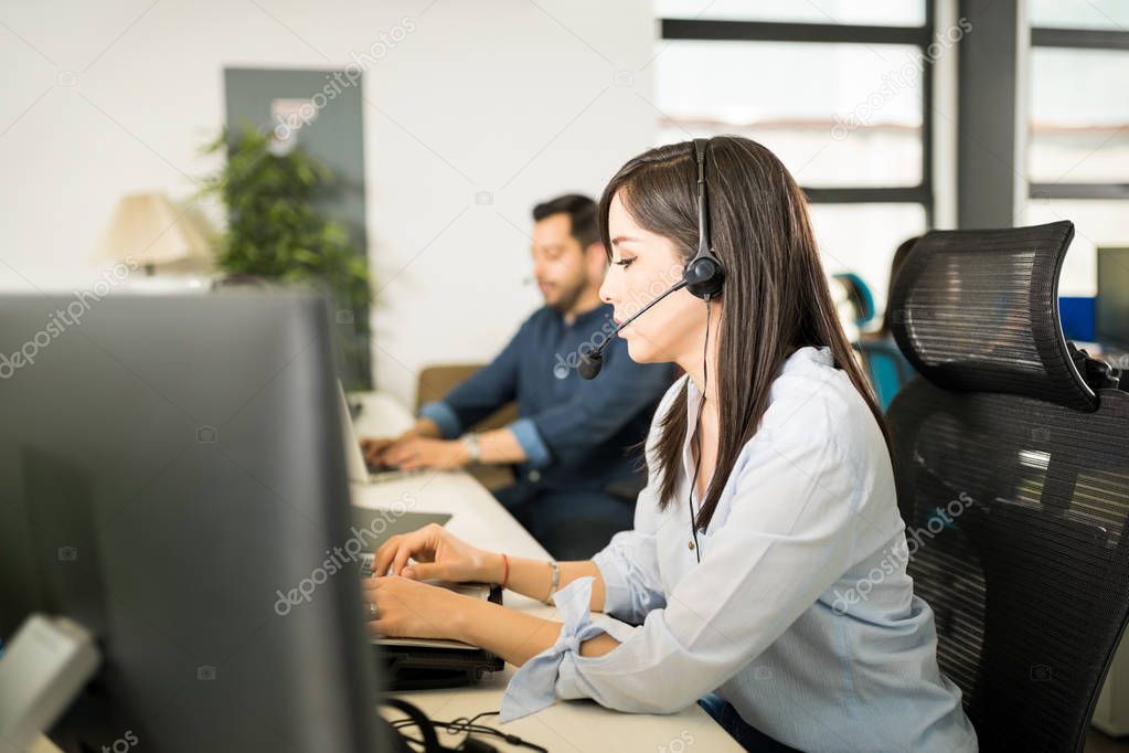 Beautiful young hispanic woman casually dressed wearing headset and taking calls from customers while working at desk in office 
