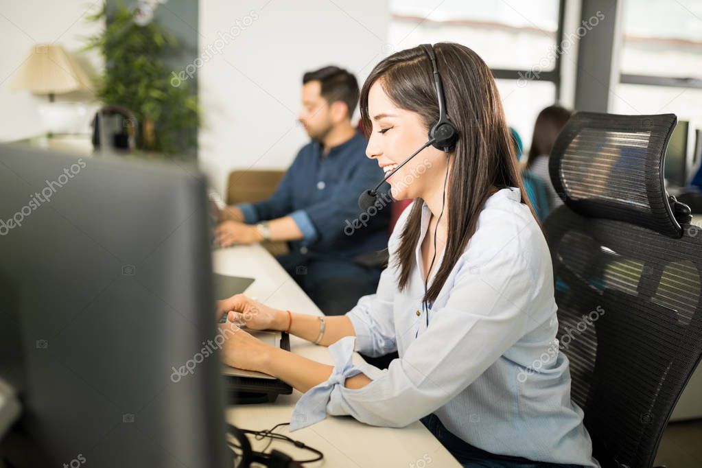 Beautiful young hispanic woman casually dressed wearing headset and taking calls from customers while working at desk in office 