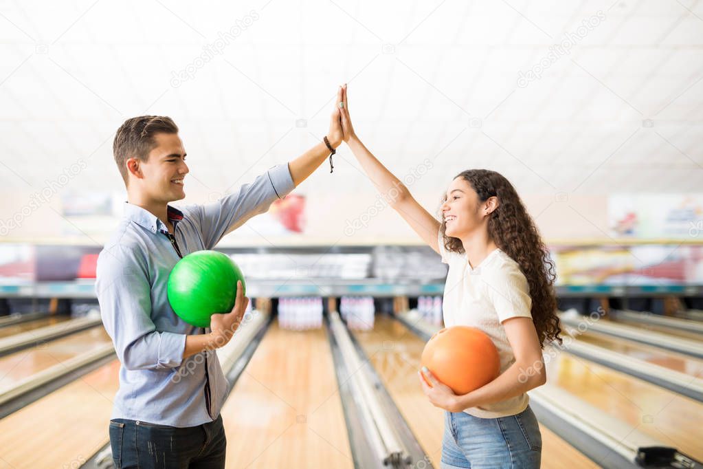 Male and female teenage friends showing team spirit with high-five at bowling alley in club