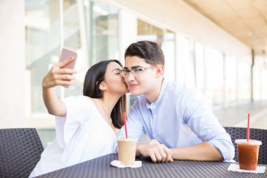 Genç kız alışveriş merkezi cep telefonuna kendi kendine portre çekerken yanağına Erkek öpüşme