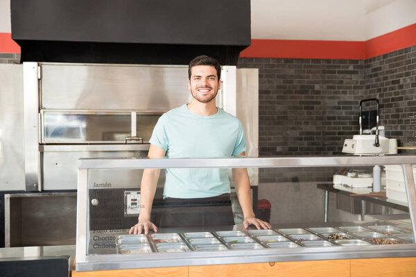 Handsome young latin entrepreneur smiling and standing welcomingly behind the order counter