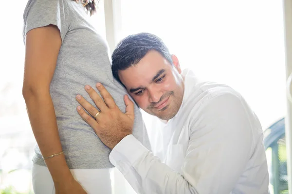 Uomo Sorridente Che Ascolta Pancia Della Donna Incinta Casa — Foto Stock