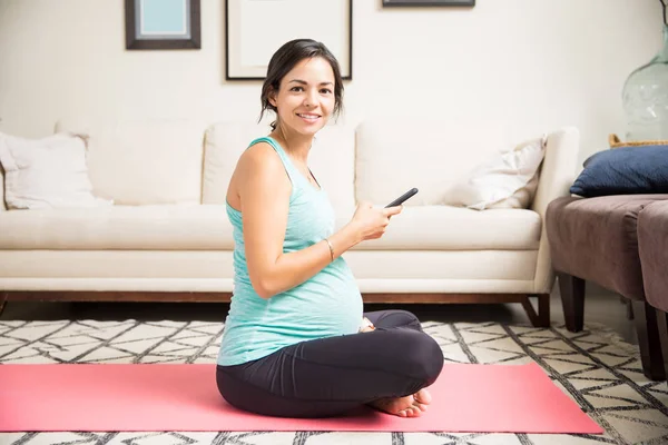 Smiling Expectant Female Holding Smartphone While Sitting Exercise Mat Home — Stock Photo, Image