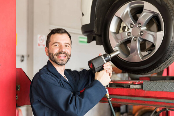 Smiling auto technician using impact gun on car tire in garage