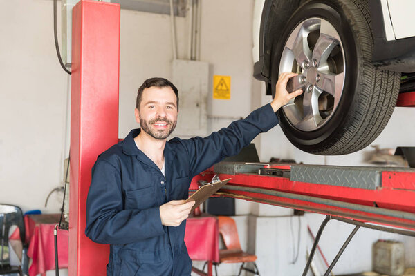 Smiling serviceman analyzing car tire while holding clipboard in workshop