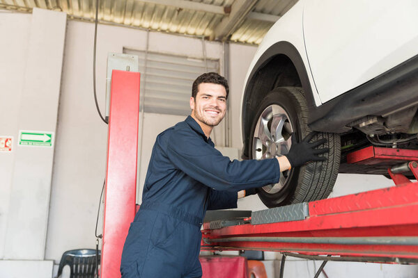 Happy serviceman removing tire while standing by hydraulic lift in garage