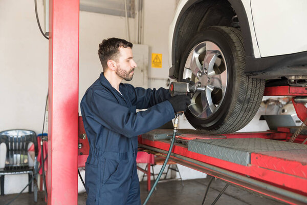 Mechanic tightening lug nuts on tire with impact wrench in auto repair shop