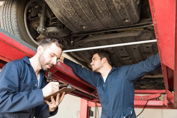 Mid Adult Mechanic Making Checklist While Coworker Measuring Tire Alignment — Stock Photo, Image