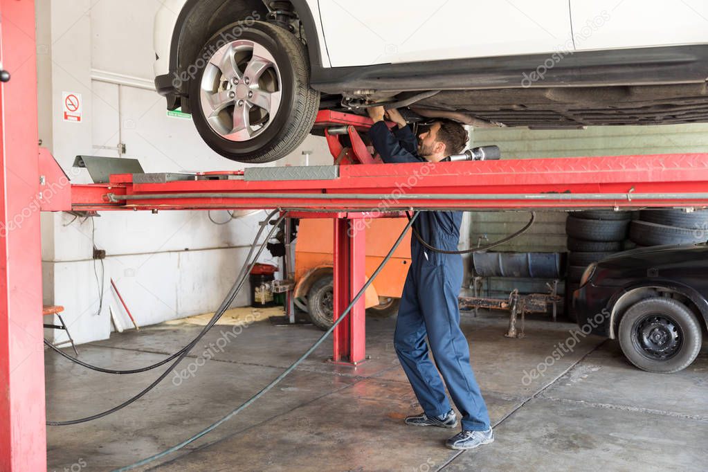 Full length of auto expert repairing car on hydraulic lift in garage