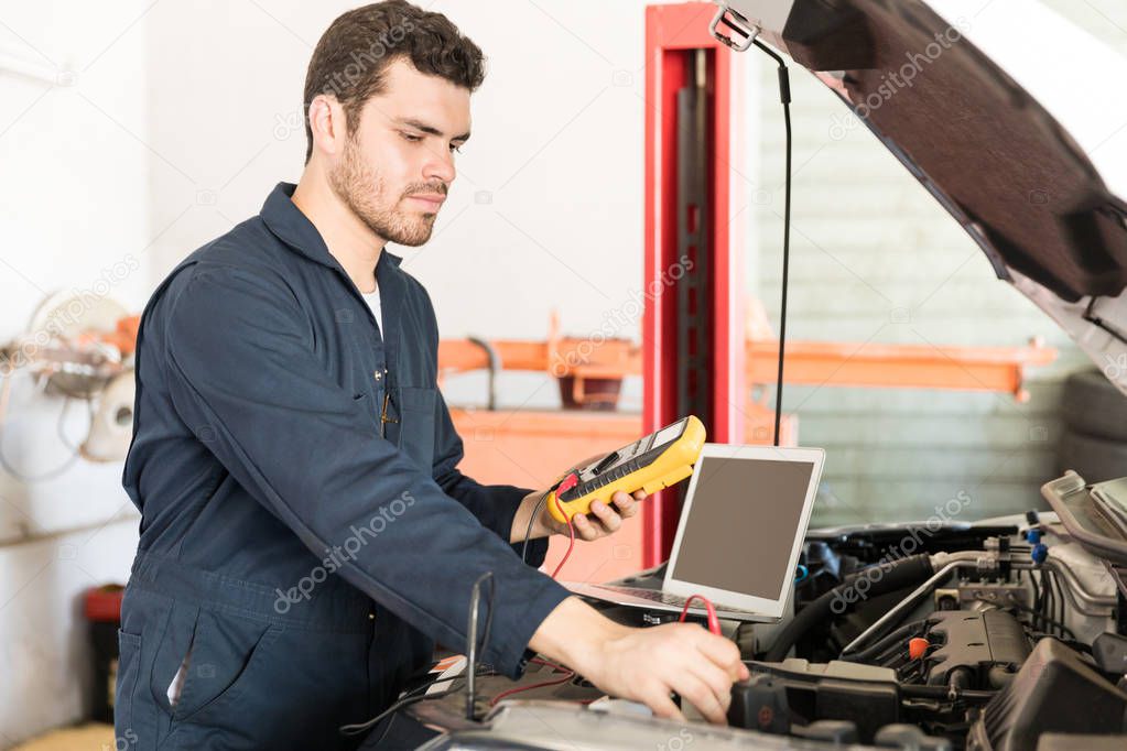 Mid adult male car mechanic checking the voltage of battery using voltmeter in garage