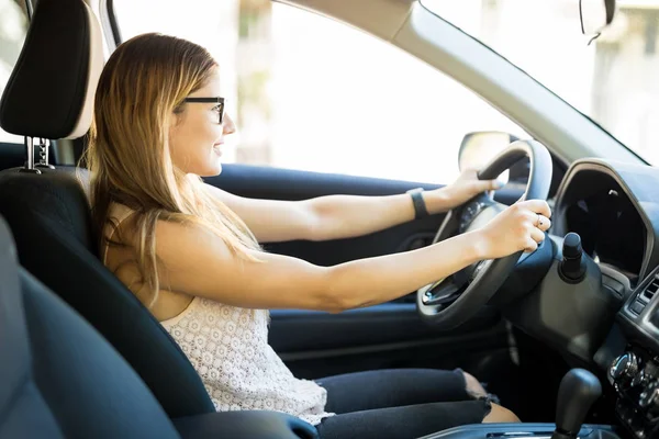 Side view of beautiful woman sitting on driving seat with both hands on steering wheel