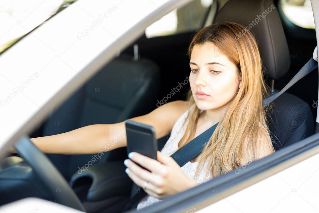 Beautiful woman driving a car and reading text message on her mobile phone