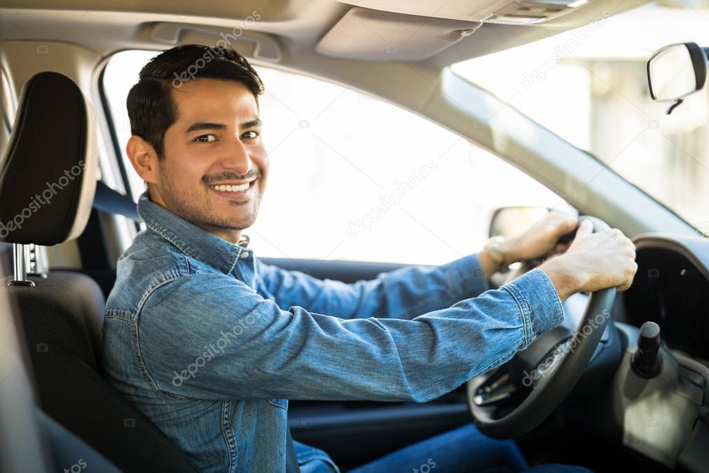 Portrait of attractive young hispanic man sitting in the driving seat of his car and making an eye contact