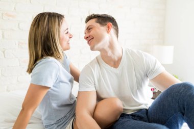 Yakışıklı yetişkin adam kadına evde yatakta otururken sevgi ile bakan orta