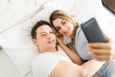 Romantik kadın ve adam evde yatakta yatıyordu süre üstünde hareket eden telefon selfie alarak yüksek açılı görünüş