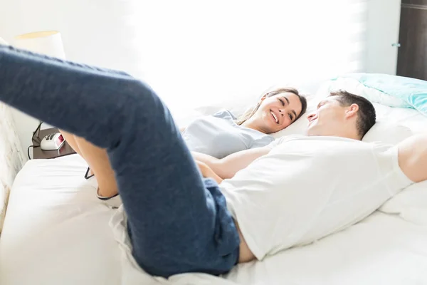 lovers with feet up smiling while lying on bed at home