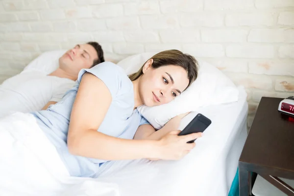 Young Woman Secretly Using Smartphone While Lying Boyfriend Bed Home — Stock Photo, Image