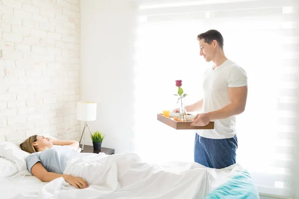 Zadowolony Mężczyzna Prowadzenia Taca Śniadaniowa Patrząc Kobiece Spanie Łóżku Domu — Zdjęcie stockowe