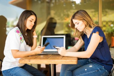 Laptop ile kafeterya masada oturan ve onların telefon fon kullanarak iki genç kadın
