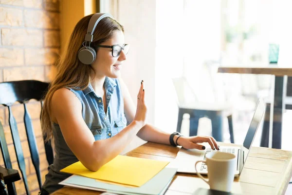 Mujer Joven Sentada Restaurante Con Auriculares Mirando Computadora Portátil Saludando —  Fotos de Stock