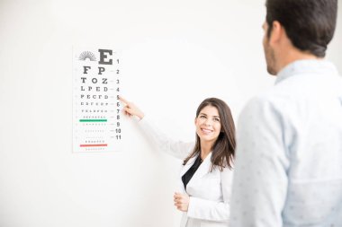 Güzel göz doktoruna duvara sıkışmış numarası ve alfabe grafik adam hasta gözleri sınamak için kullanma
