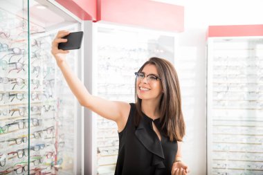 Gözlükçü alışveriş ayakta üzerinde çekici kadın portresi depolamak, trendy gözlük selfie alarak ve gülümseyen