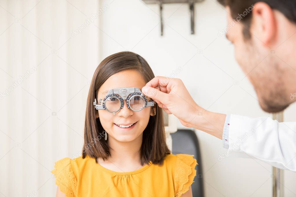 Closeup hand of optometrist with trial frame checking girl patient vision at optics store