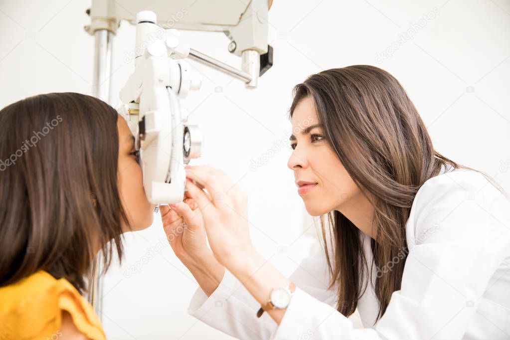 Pretty optometrist adjusting phoropter for child patient in store