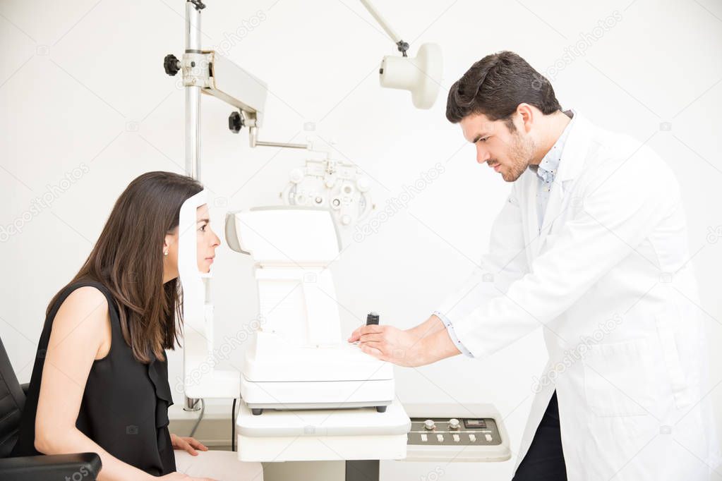 Experienced optician doing eye checkup to young woman on slit lamp machine in laboratory