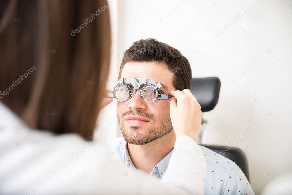 Female optician adjusting lens of trial frames on mature man