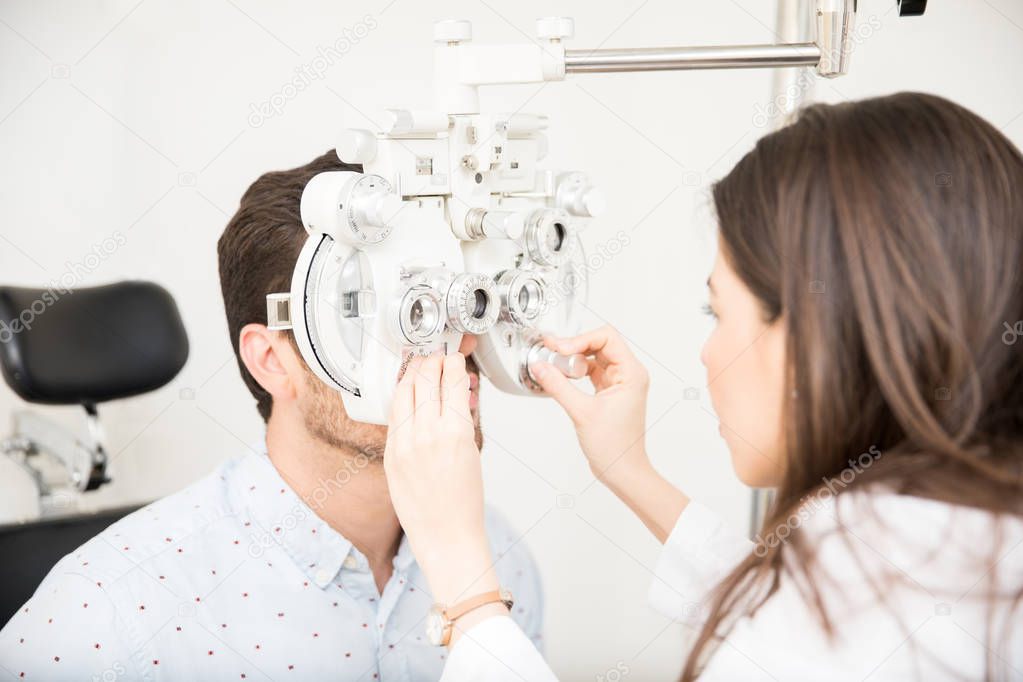 Beautiful woman optometrist performing eye checkup with phoropter at clinic