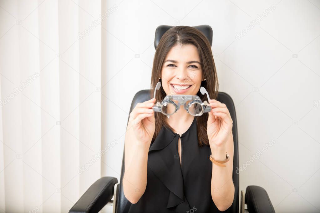 Portrait of beautiful woman in black dress holding trial frames ready to wear for eyesight test in clinic