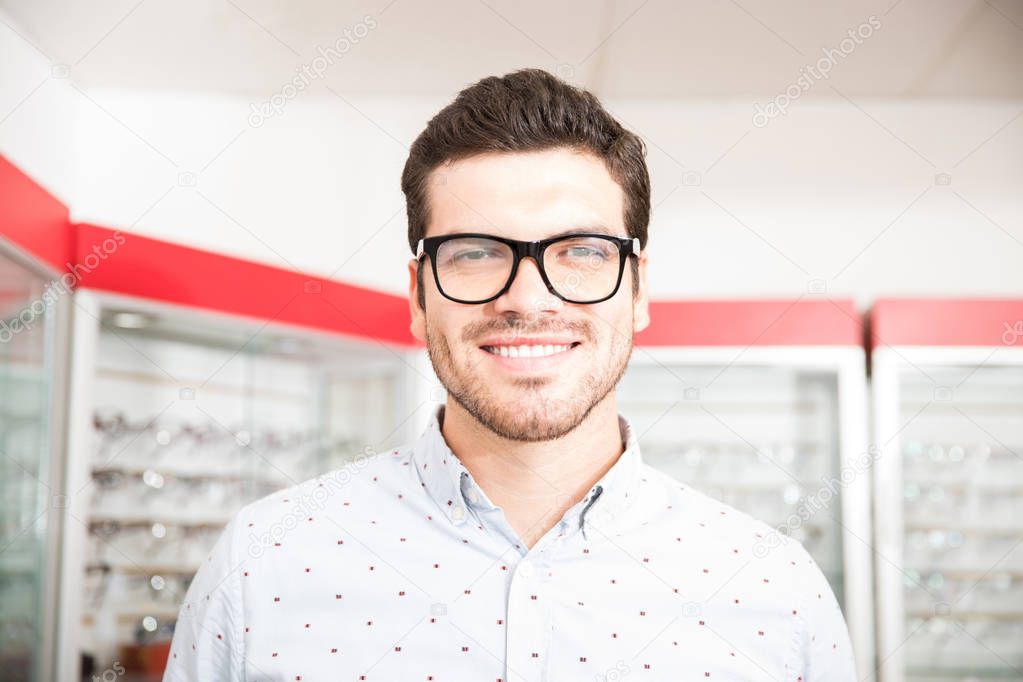 Portrait of handsome man in glasses looking at camera while standing in optician shop