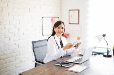 Güzel İspanyol kadın doktor bir göz teması yapma bir dijital tablet ile onun Kliniği'nde oturan portresi