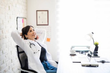 Ellerini başının arkasında ile geri eğilerek rahat İspanyol kadın doktor portresi