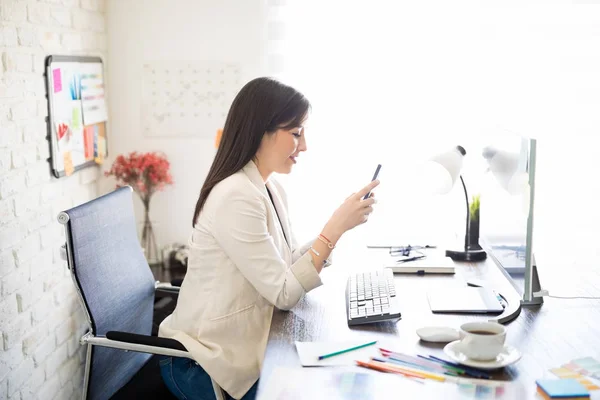 Onun Ofis Masası Spanyol Kadın Tasarımcı Oturan Akıllı Telefon Kullanarak — Stok fotoğraf