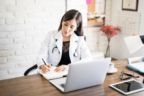 Médica Mulher Escrevendo Livro Enquanto Sentada Sua Mesa — Fotografia de Stock