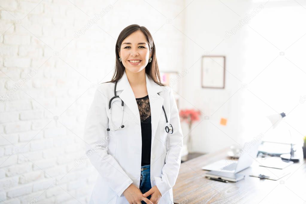 Portrait of pretty young latin female doctor standing in her clinic and making an eye contact
